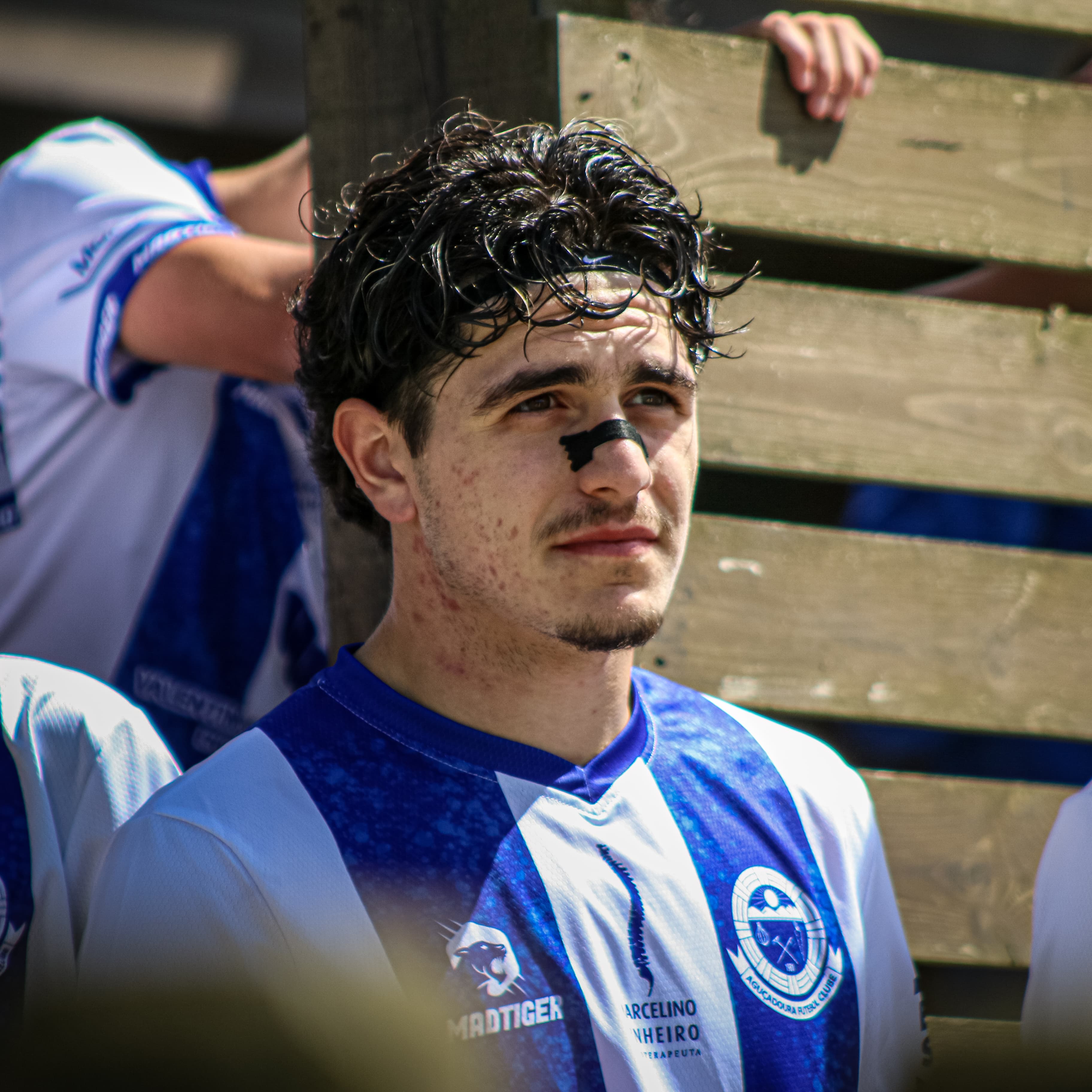 Jogador de futebol com fita no nariz e cabelo encaracolado vestindo uniforme azul e branco.