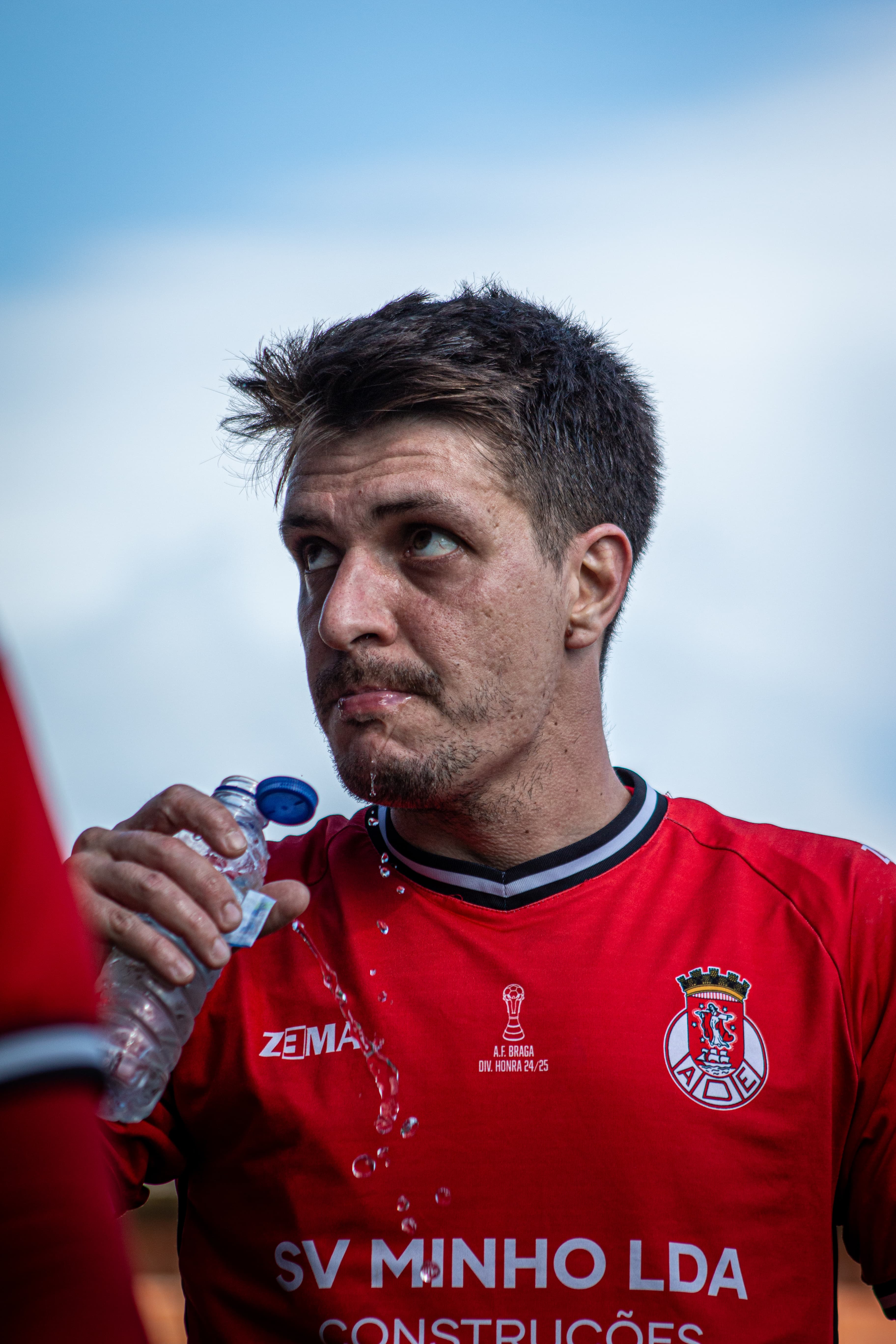 Jogador de futebol com camisola vermelha olha para cima enquanto a água escorre do queixo.