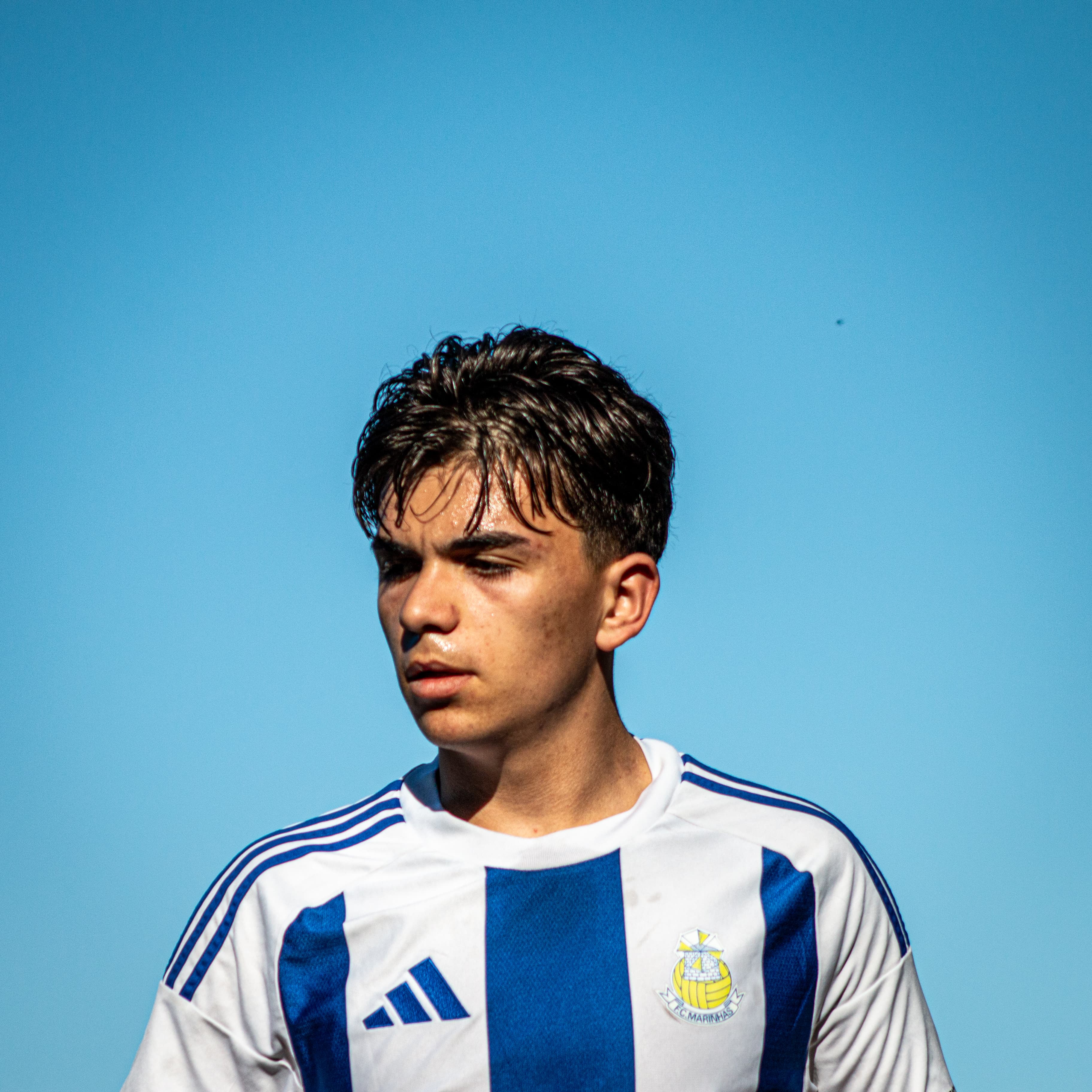 Jovem jogador de futebol em camisola listrada azul e branca sob um céu azul limpo.